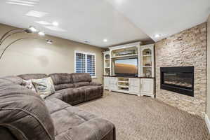 Recessed lighting illuminates a carpeted living space featuring a built-in media center with shelving and an integrated fireplace with a stacked stone surround