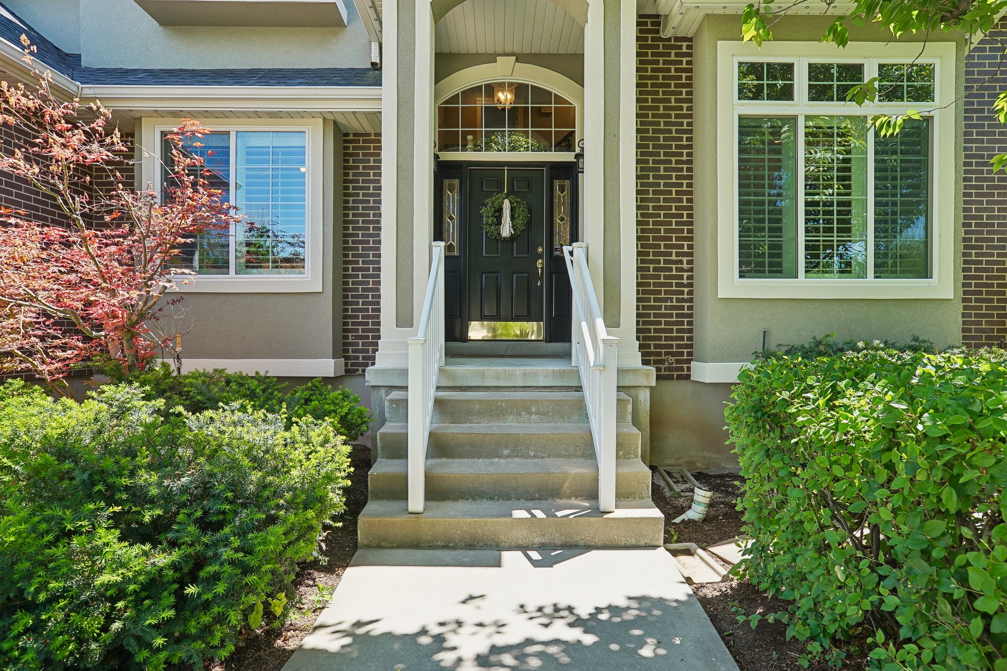 Brick and stucco facade with a covered entry, concrete steps, white railings, and a dark front door with an arched transom window