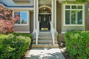 Brick and stucco facade with a covered entry, concrete steps, white railings, and a dark front door with an arched transom window