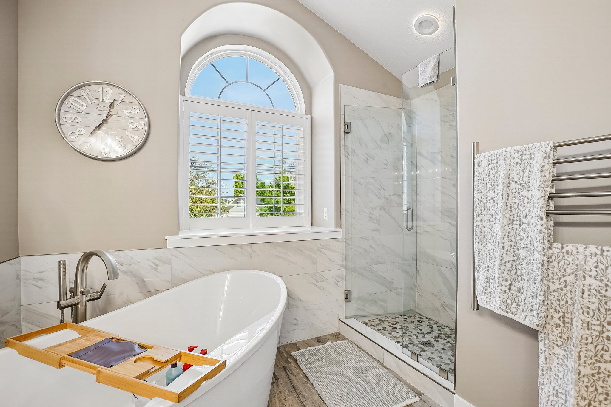 Freestanding soaking tub with floor-mounted faucet, complemented by a glass-enclosed shower with pebble tile flooring