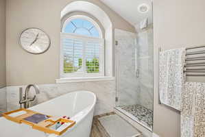 Freestanding soaking tub with floor-mounted faucet, complemented by a glass-enclosed shower with pebble tile flooring