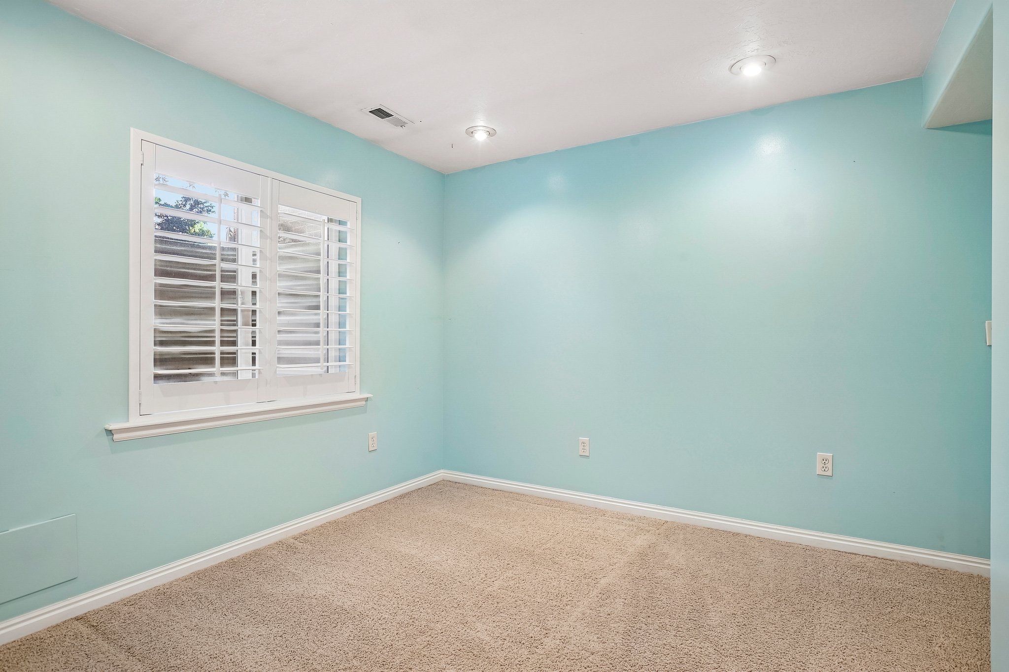 Bright room featuring a window with plantation shutters, recessed lighting, neutral carpet, and white baseboards