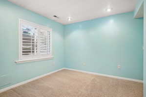 Bright room featuring a window with plantation shutters, recessed lighting, neutral carpet, and white baseboards