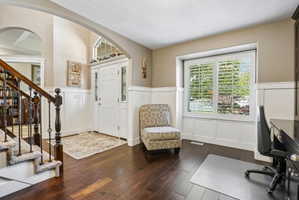 Inviting entryway featuring dark wood-finish flooring, white board and batten paneling, and an arched doorway