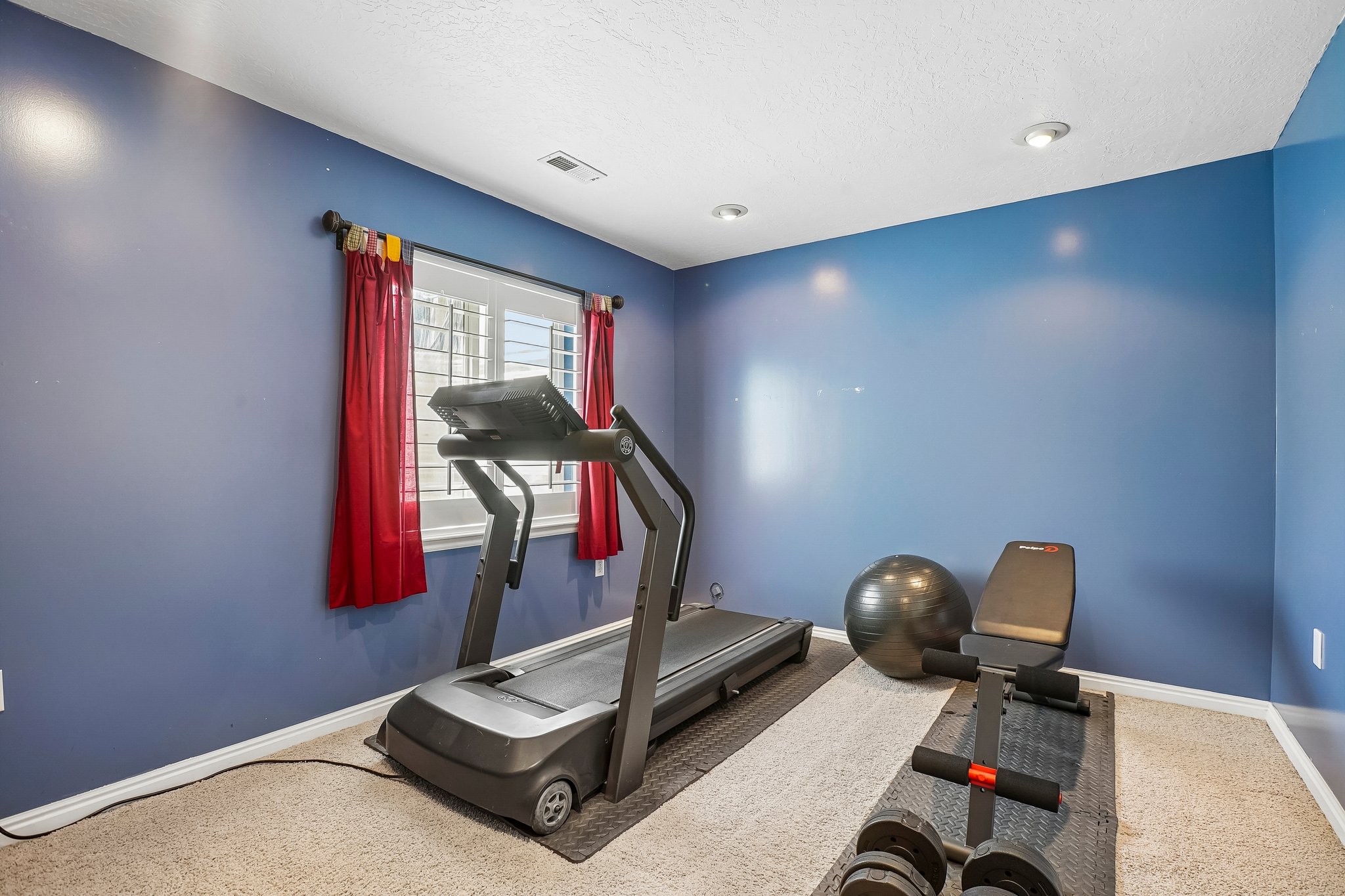 Carpeted room featuring a window with white blinds and red drapes, recessed lighting, and blue painted walls