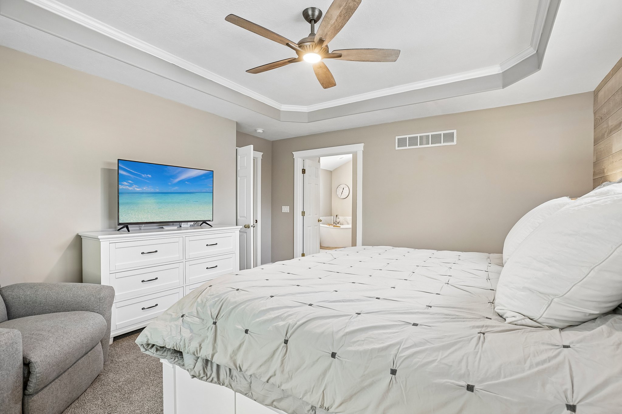 Bedroom featuring a tray ceiling with crown molding, a ceiling fan with wood-finish blades, and a textured accent wall