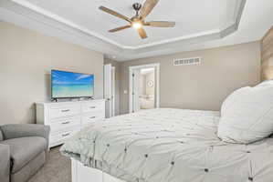 Bedroom featuring a tray ceiling with crown molding, a ceiling fan with wood-finish blades, and a textured accent wall