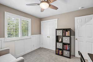 Carpeted room featuring a ceiling fan with light, white wainscoting, and a window with plantation shutters