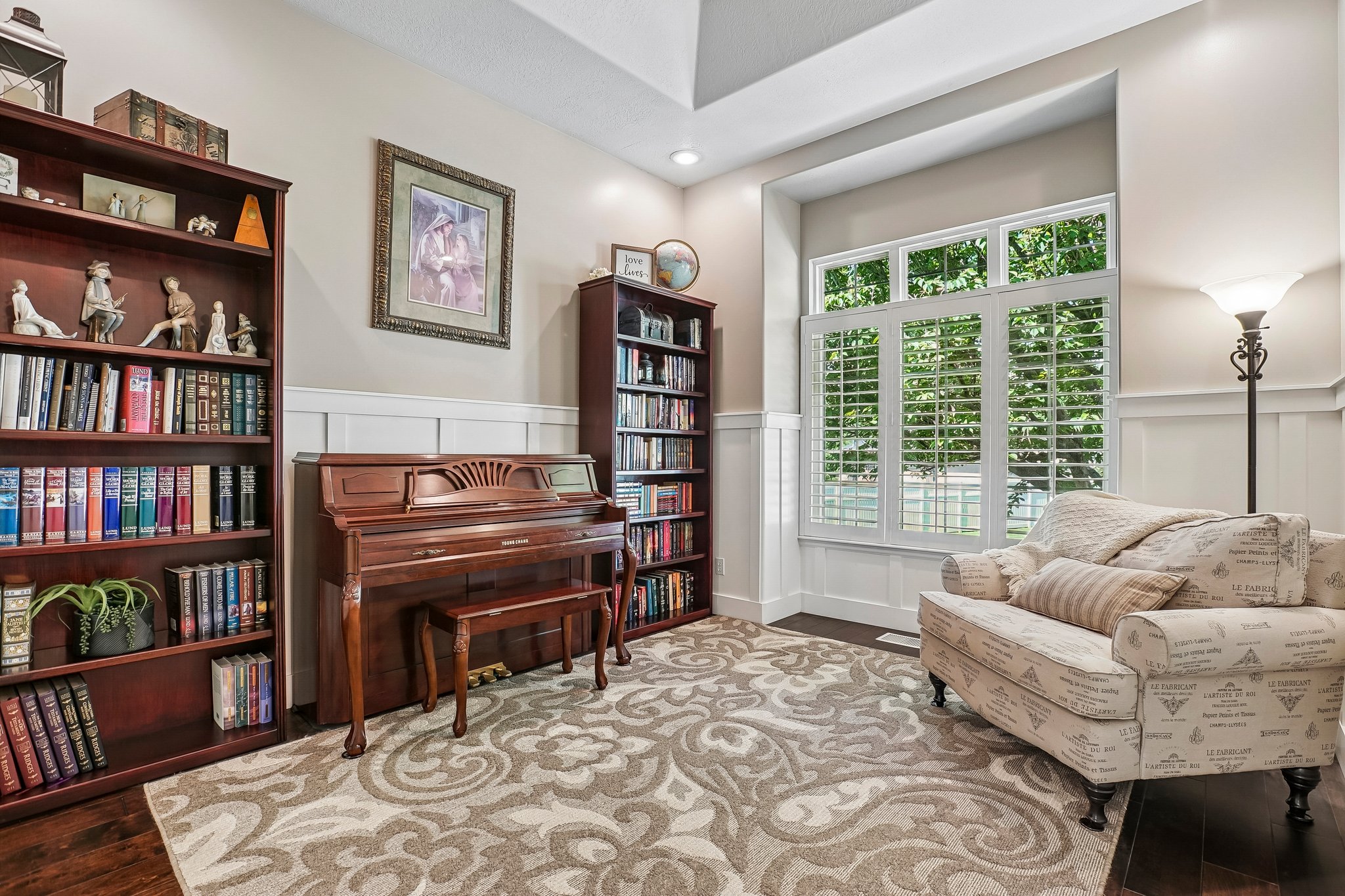 A dedicated room featuring rich wood-finish flooring, wainscoting, and large windows with plantation shutters