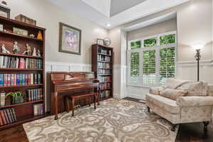 A dedicated room featuring rich wood-finish flooring, wainscoting, and large windows with plantation shutters