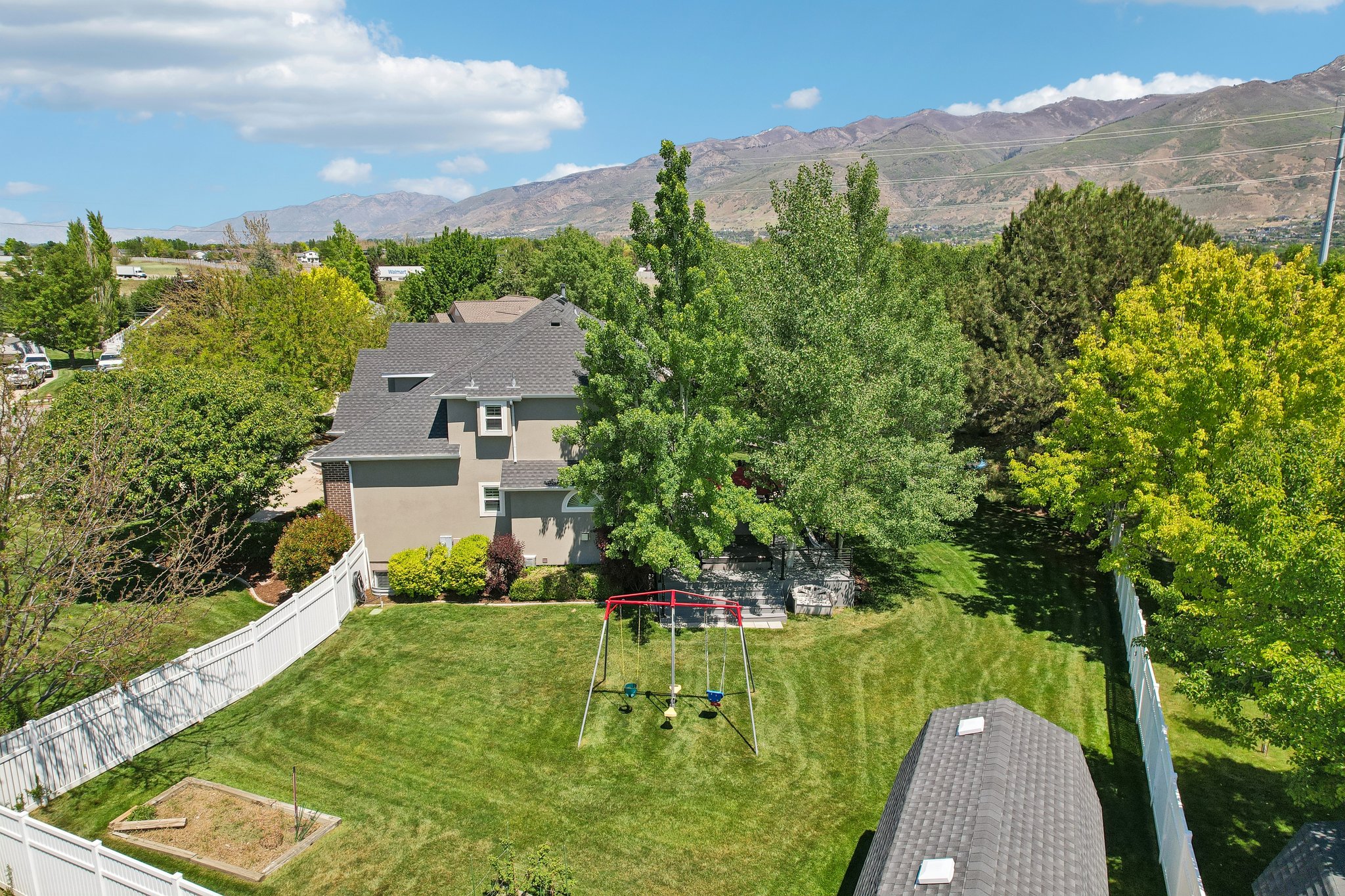 Expansive fenced backyard featuring a manicured lawn, mature trees, and a built-in garden bed