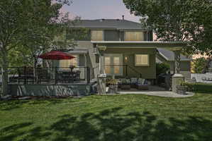 Expansive backyard featuring a manicured lawn, a raised outdoor deck with cable railing, a covered patio area, and mature trees providing shade