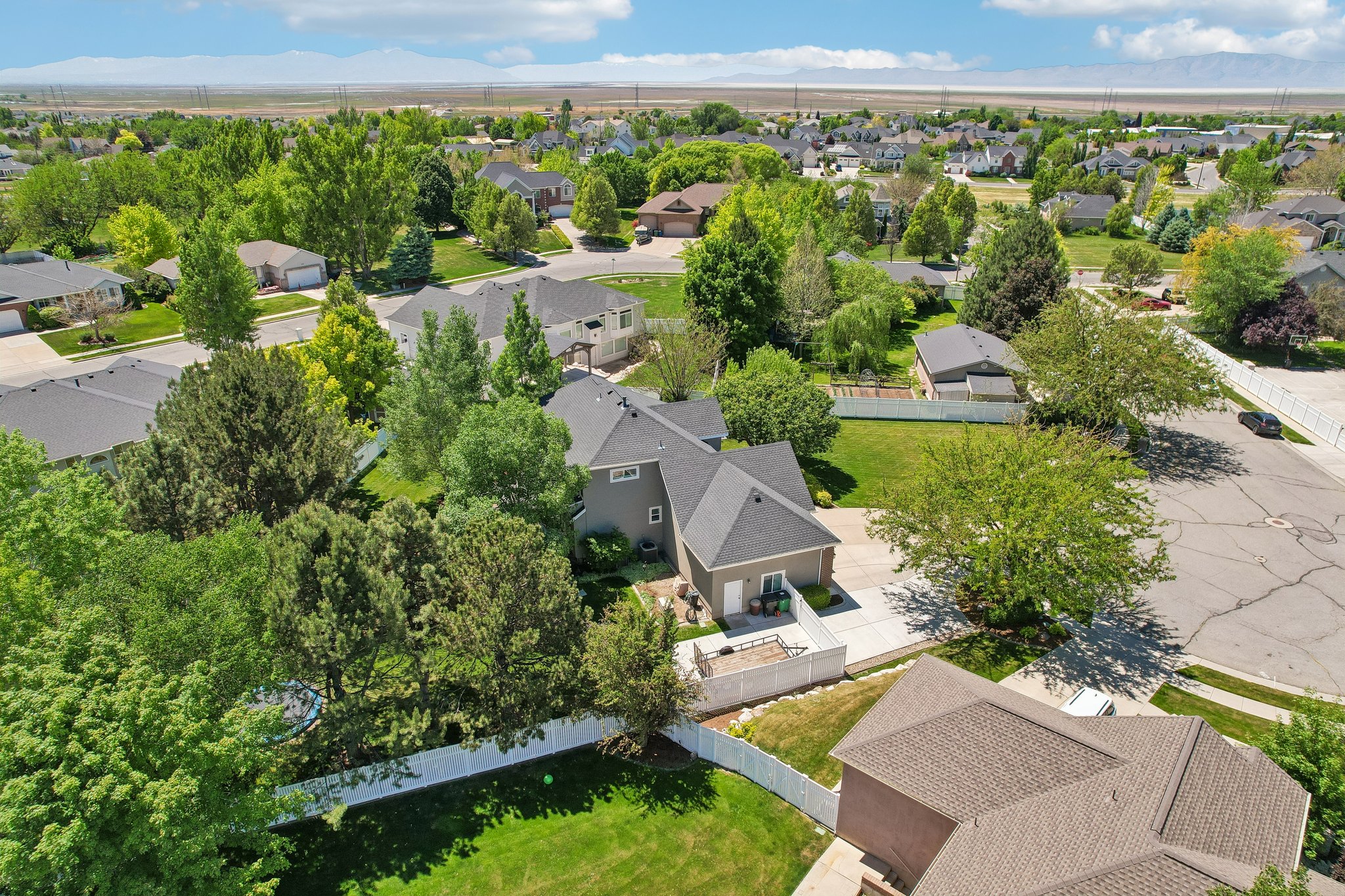 Residential property featuring a grey exterior, dark shingle roof, attached garage, and white fencing