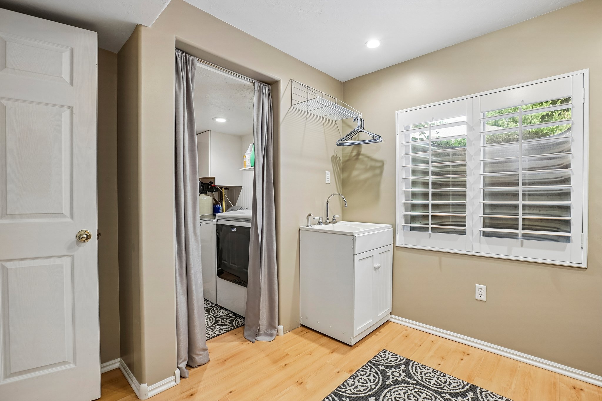 Dedicated laundry area featuring a utility sink with a cabinet base, wood-finish flooring, and white plantation shutters