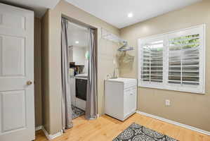Dedicated laundry area featuring a utility sink with a cabinet base, wood-finish flooring, and white plantation shutters