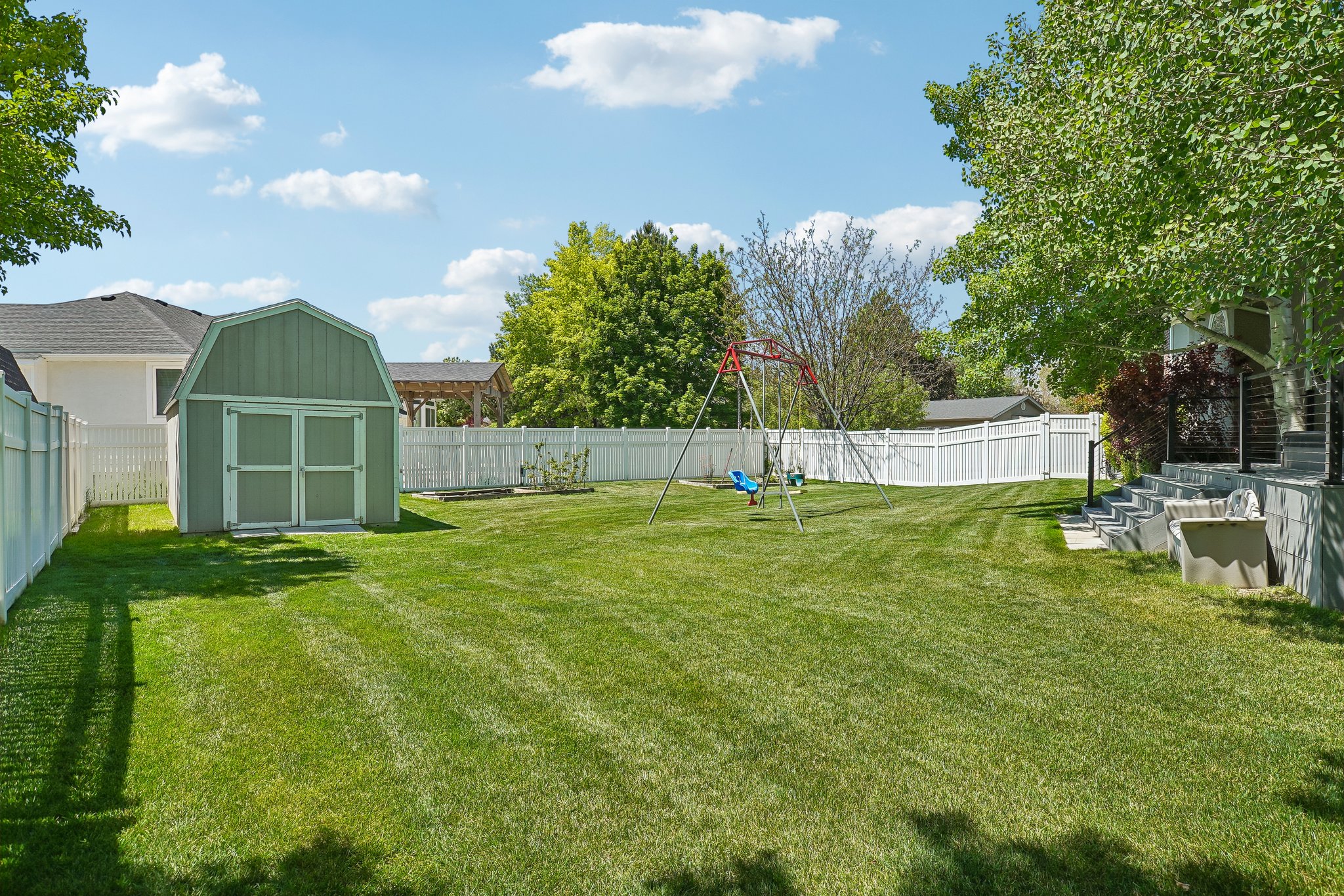 Expansive rear yard featuring a large lawn area, a green barn-style storage shed, and a white privacy fence