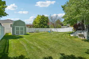 Expansive rear yard featuring a large lawn area, a green barn-style storage shed, and a white privacy fence