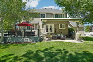 Expansive backyard featuring a manicured lawn, a raised composite deck with cable railing, a ground-level concrete patio, and mature trees providing shade