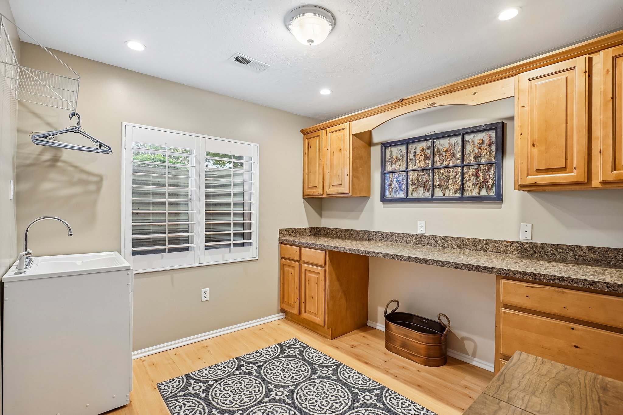 Utility room featuring wood-finish flooring, a utility sink with a high-arc faucet, and plantation shutters