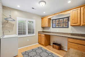 Utility room featuring wood-finish flooring, a utility sink with a high-arc faucet, and plantation shutters