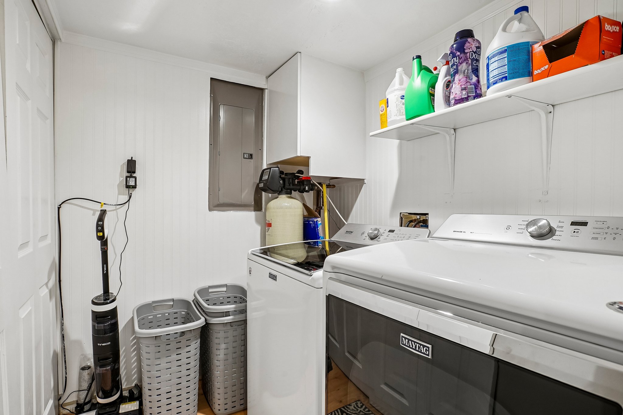 Dedicated laundry area featuring white wall paneling, built-in shelving, and a water filtration system