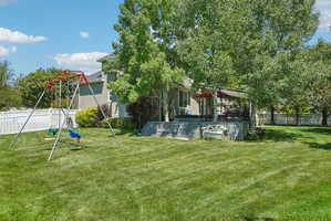 Expansive grassy backyard featuring a white picket fence, mature trees, and a multi-level deck with a covered patio area