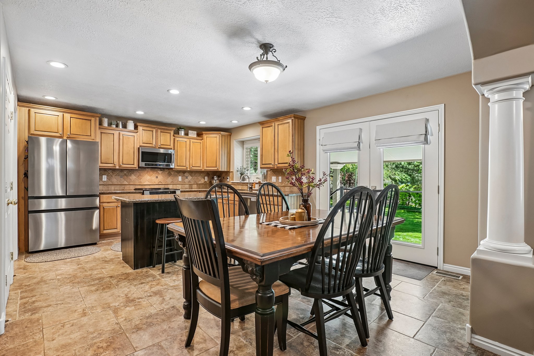 Open-concept kitchen and dining area featuring light wood cabinetry, stainless steel appliances, a center island with a dark finish, and tiled flooring