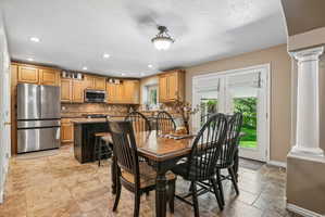Open-concept kitchen and dining area featuring light wood cabinetry, stainless steel appliances, a center island with a dark finish, and tiled flooring