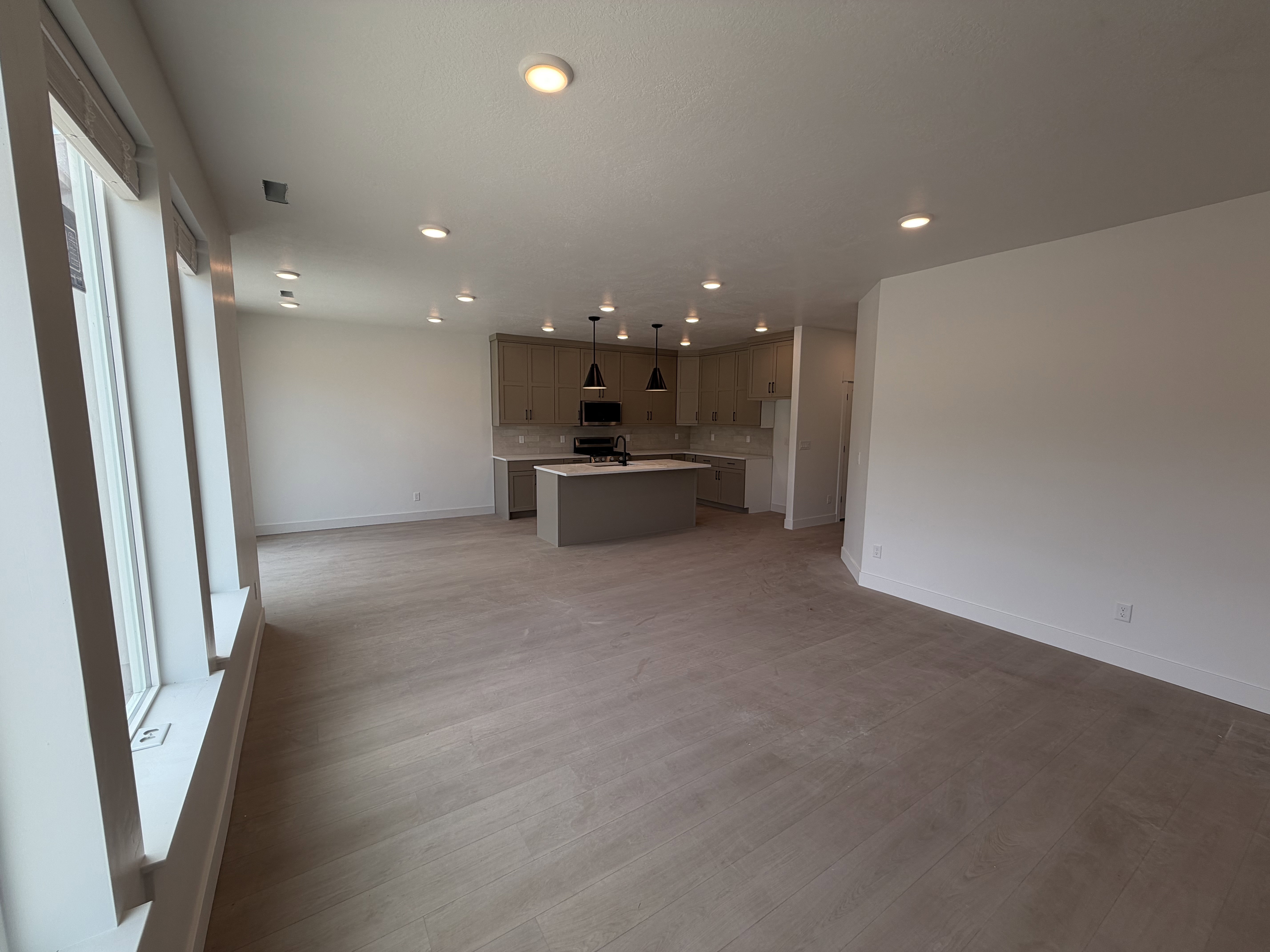 Spacious room featuring wood-finish flooring, ample natural light from large windows, recessed ceiling lighting, a kitchen with light cabinetry, and an island with pendant lighting