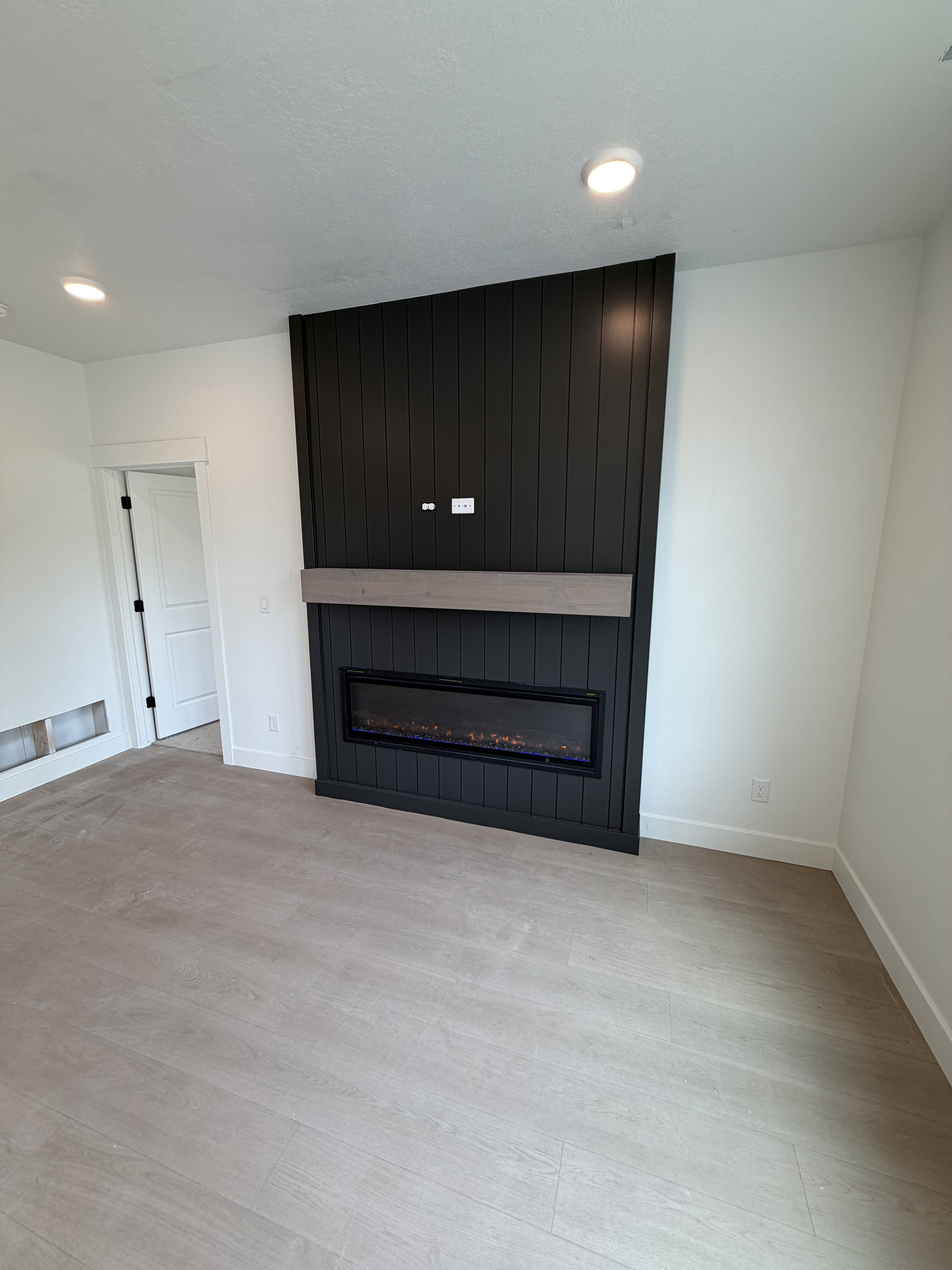 Modern fireplace feature wall with vertical black paneling and a light wood-finish mantel