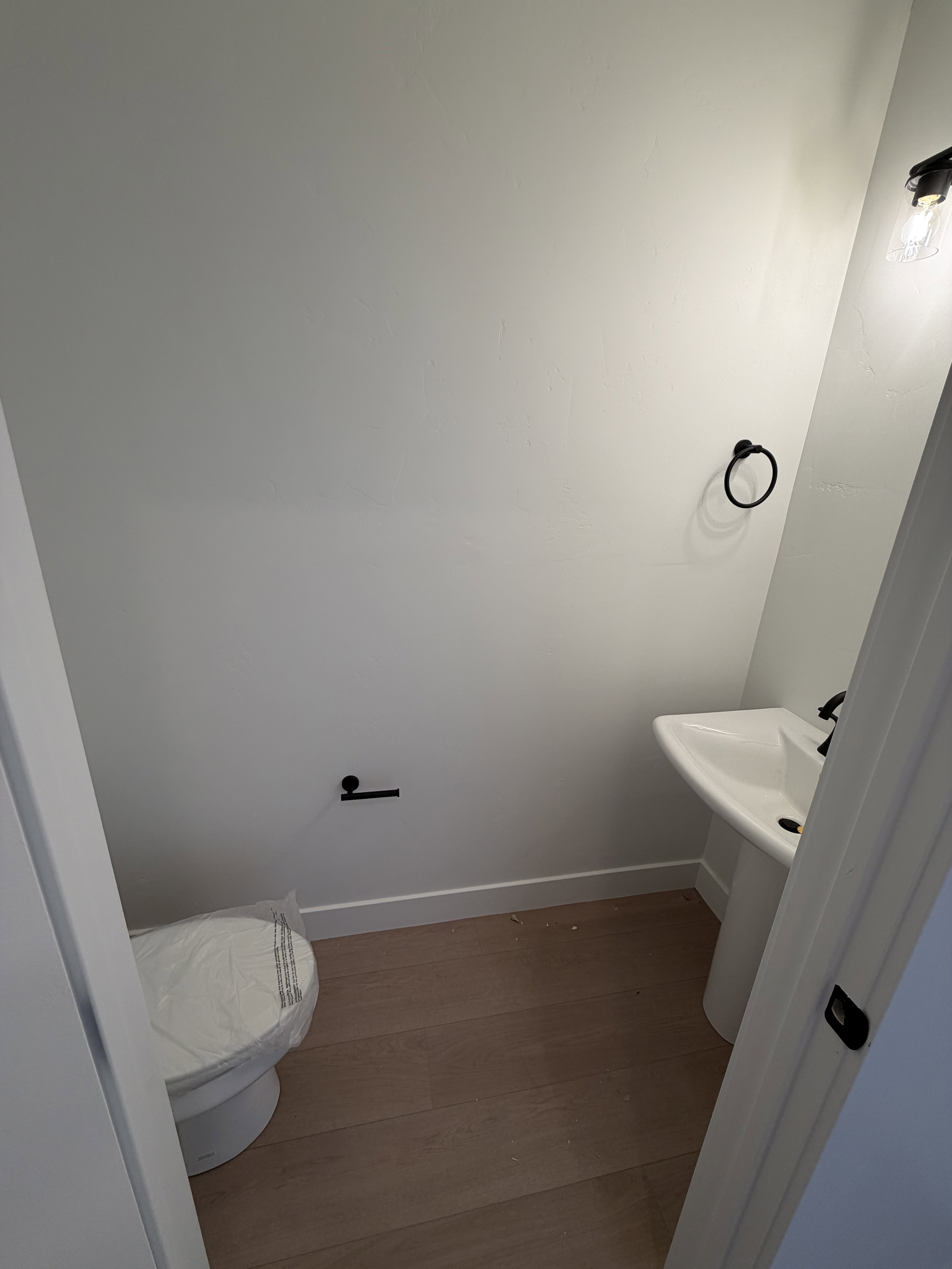 Powder room featuring light wood-finish flooring, a white pedestal sink with a matte black faucet, and a white toilet