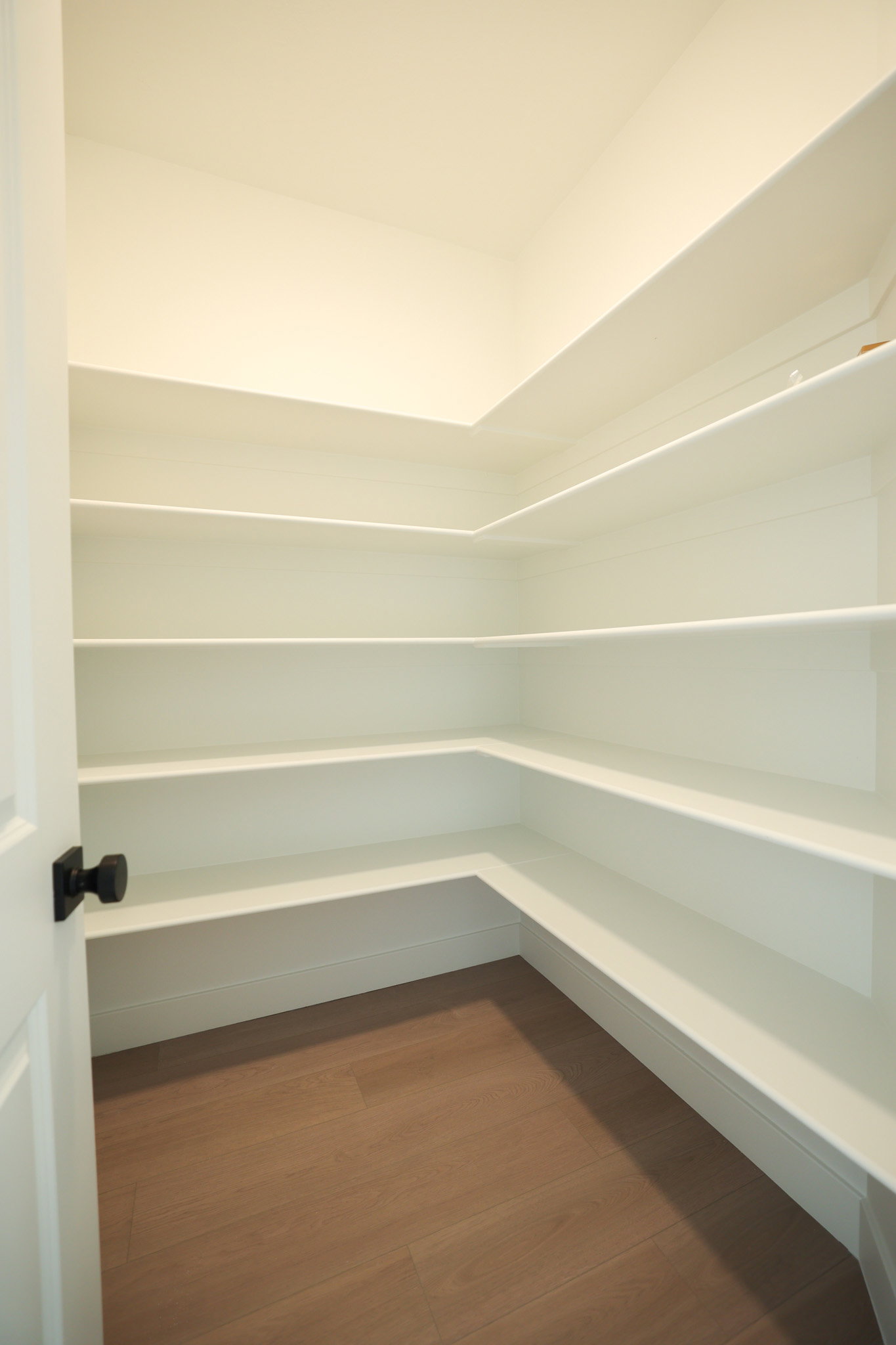 Walk-in pantry featuring extensive white shelving and wood-finish flooring