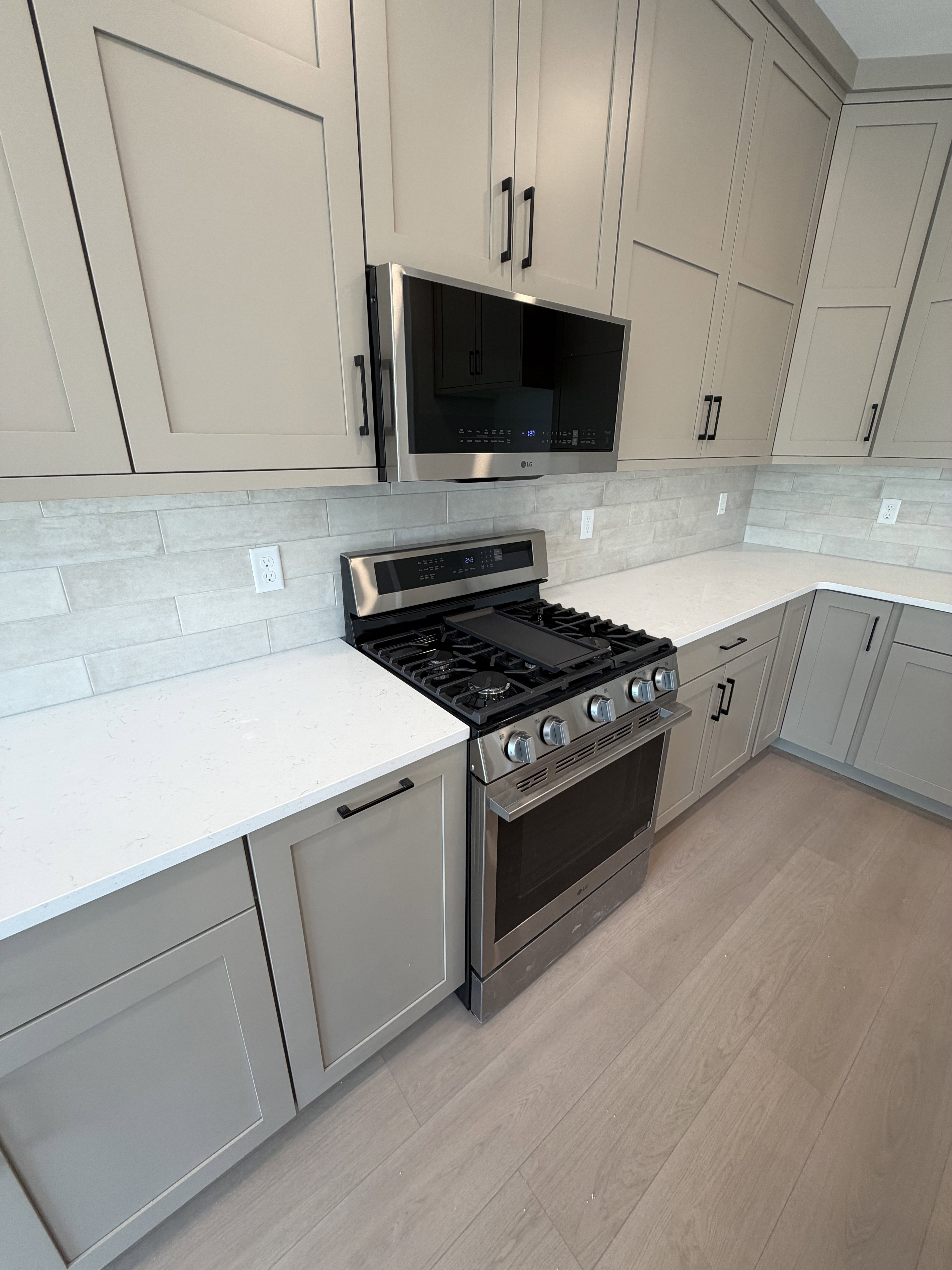 Contemporary kitchen featuring light gray cabinetry, stainless steel range with griddle, over-the-range microwave, quartz countertops, and wood-finish flooring