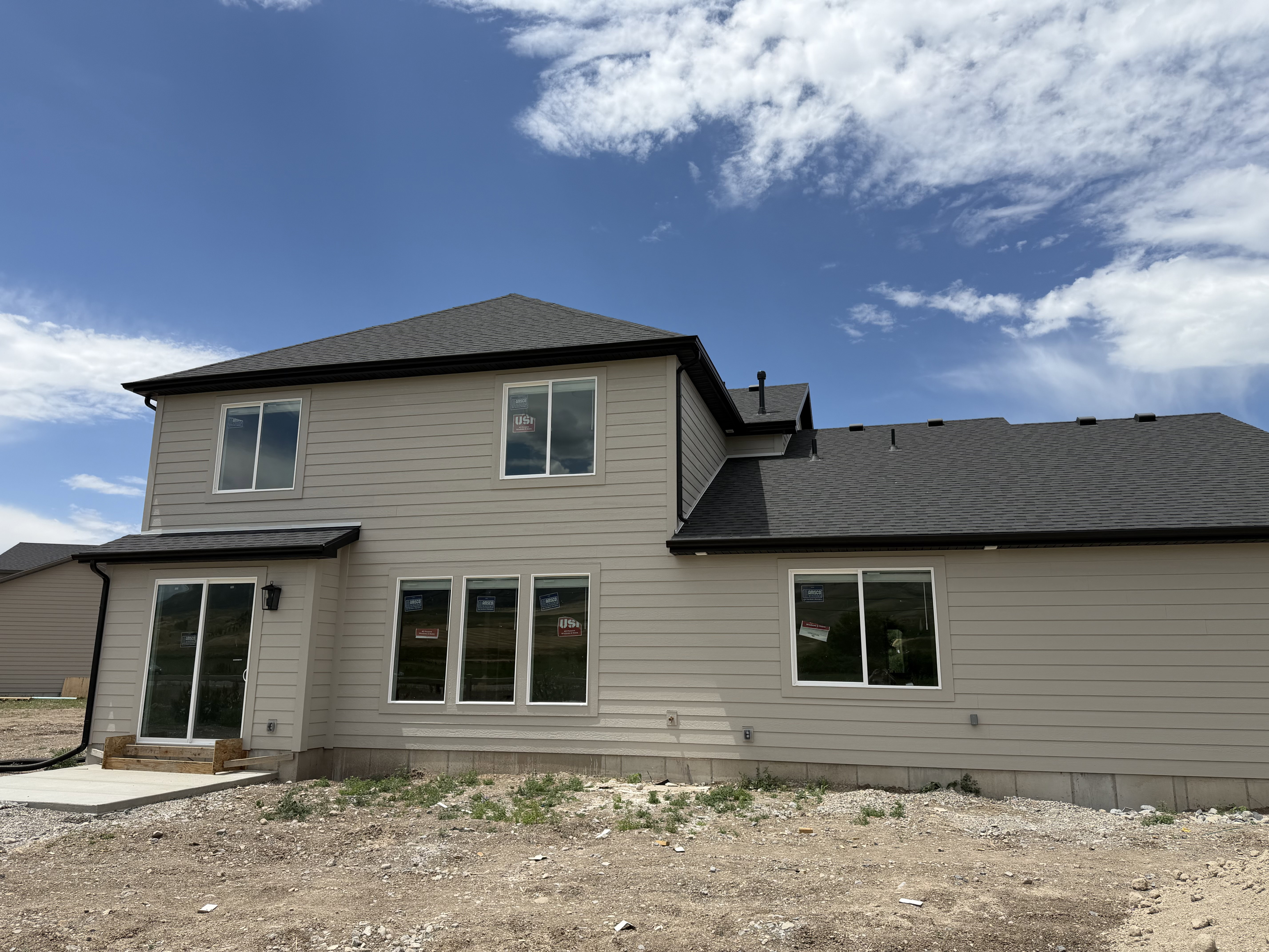 Rear exterior featuring beige horizontal siding, a dark shingle roof, and multiple white-framed windows