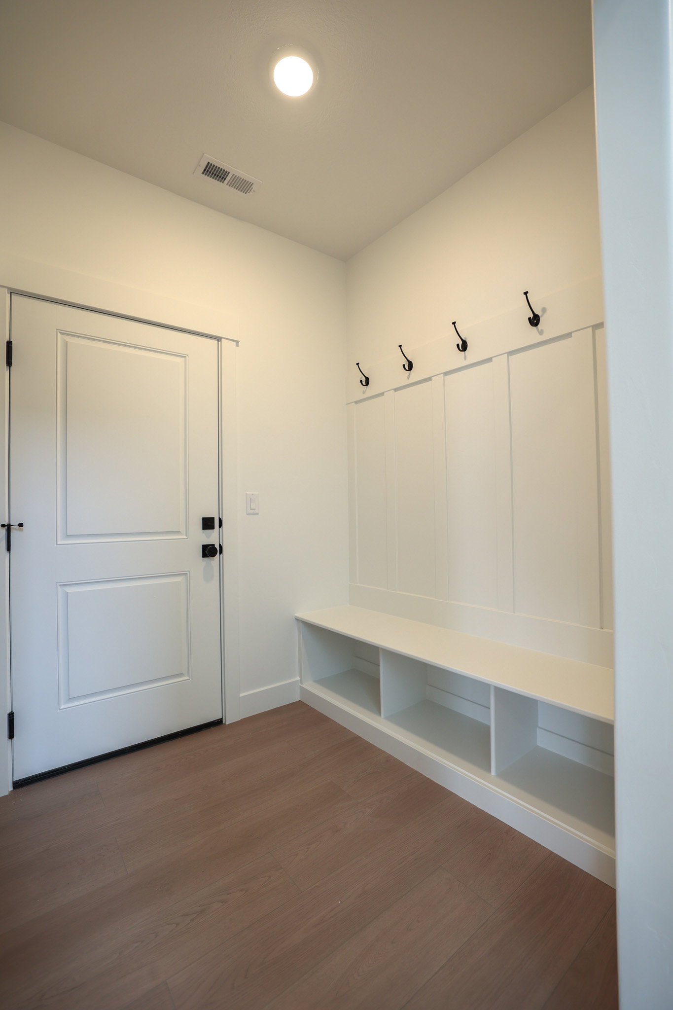 Entryway featuring wood-finish flooring, a white paneled door with black hardware, and a built-in bench with storage cubbies