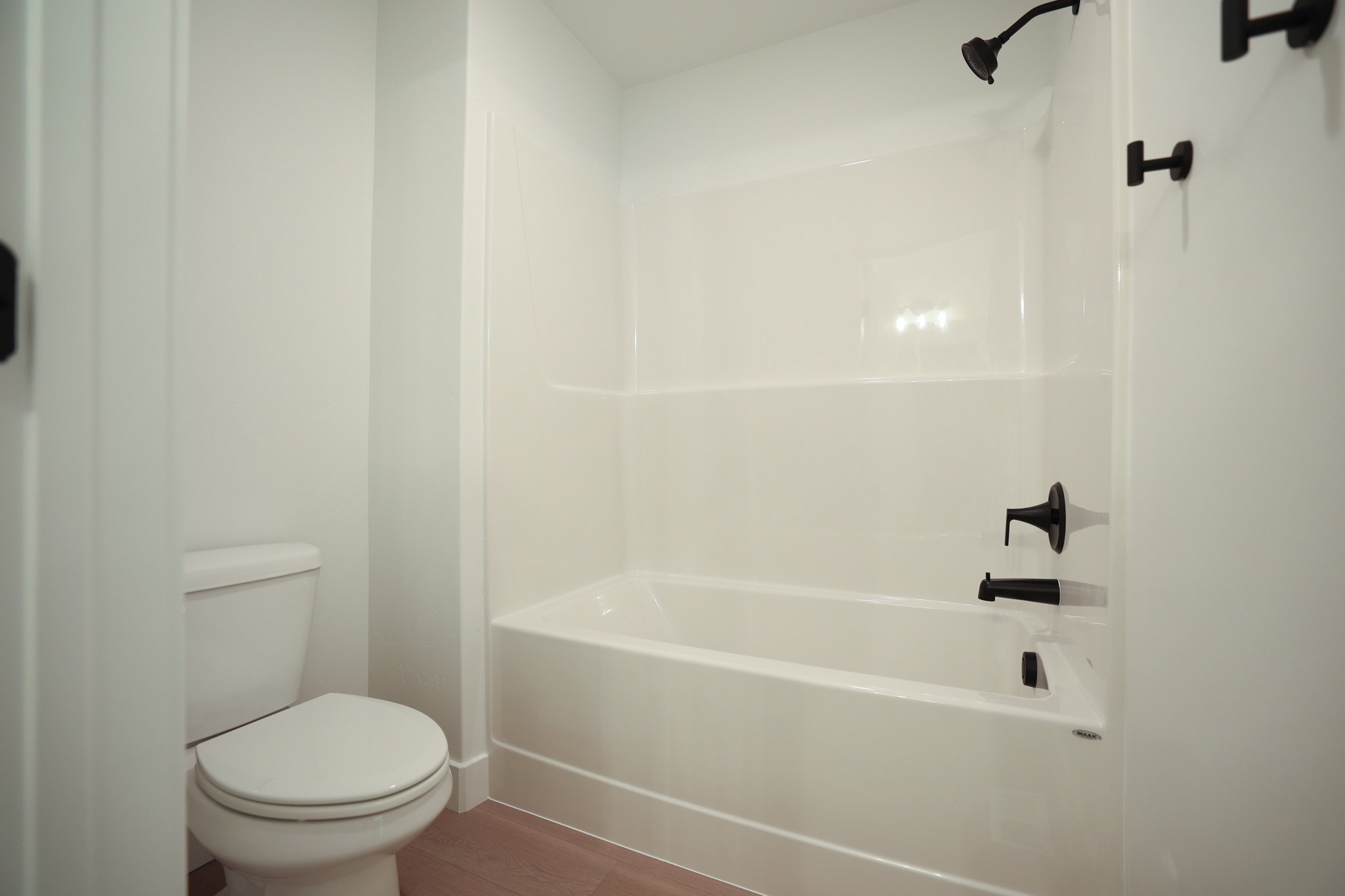 Full bathroom featuring a white tub and shower combination with matte black fixtures, a white toilet, and wood-finish flooring