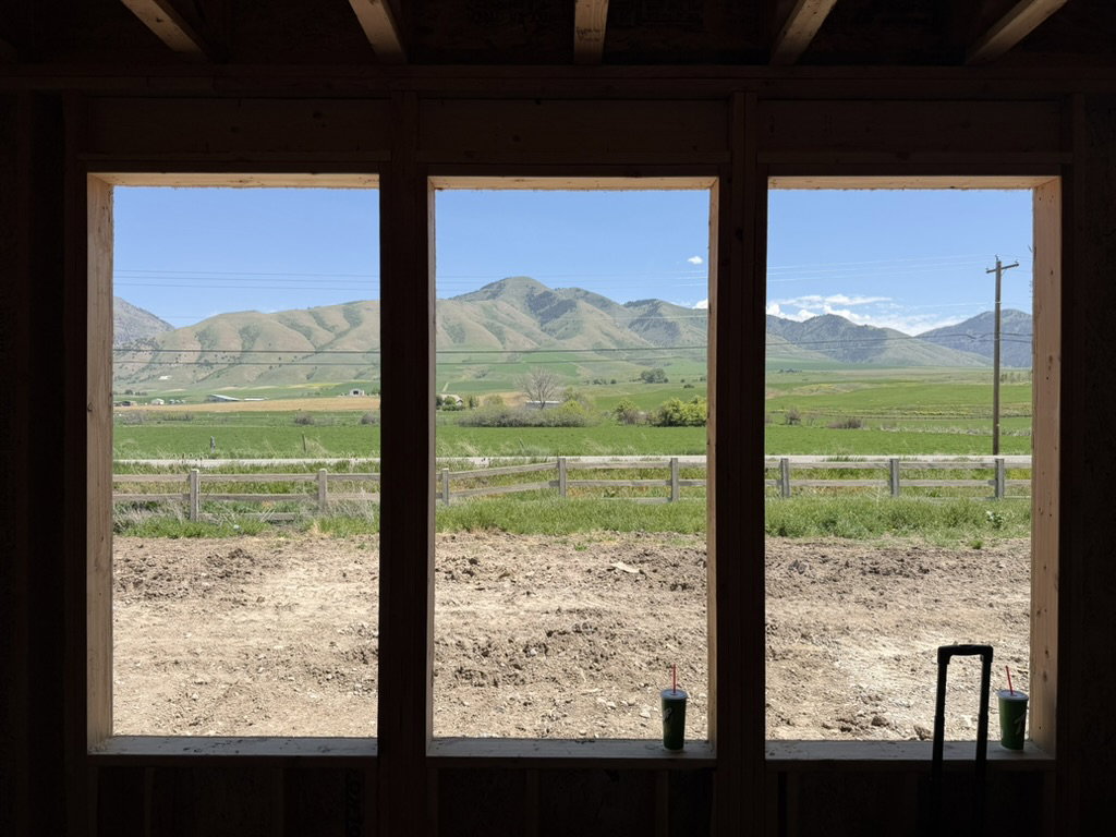 Multiple window openings showcasing distant mountains and expansive green fields