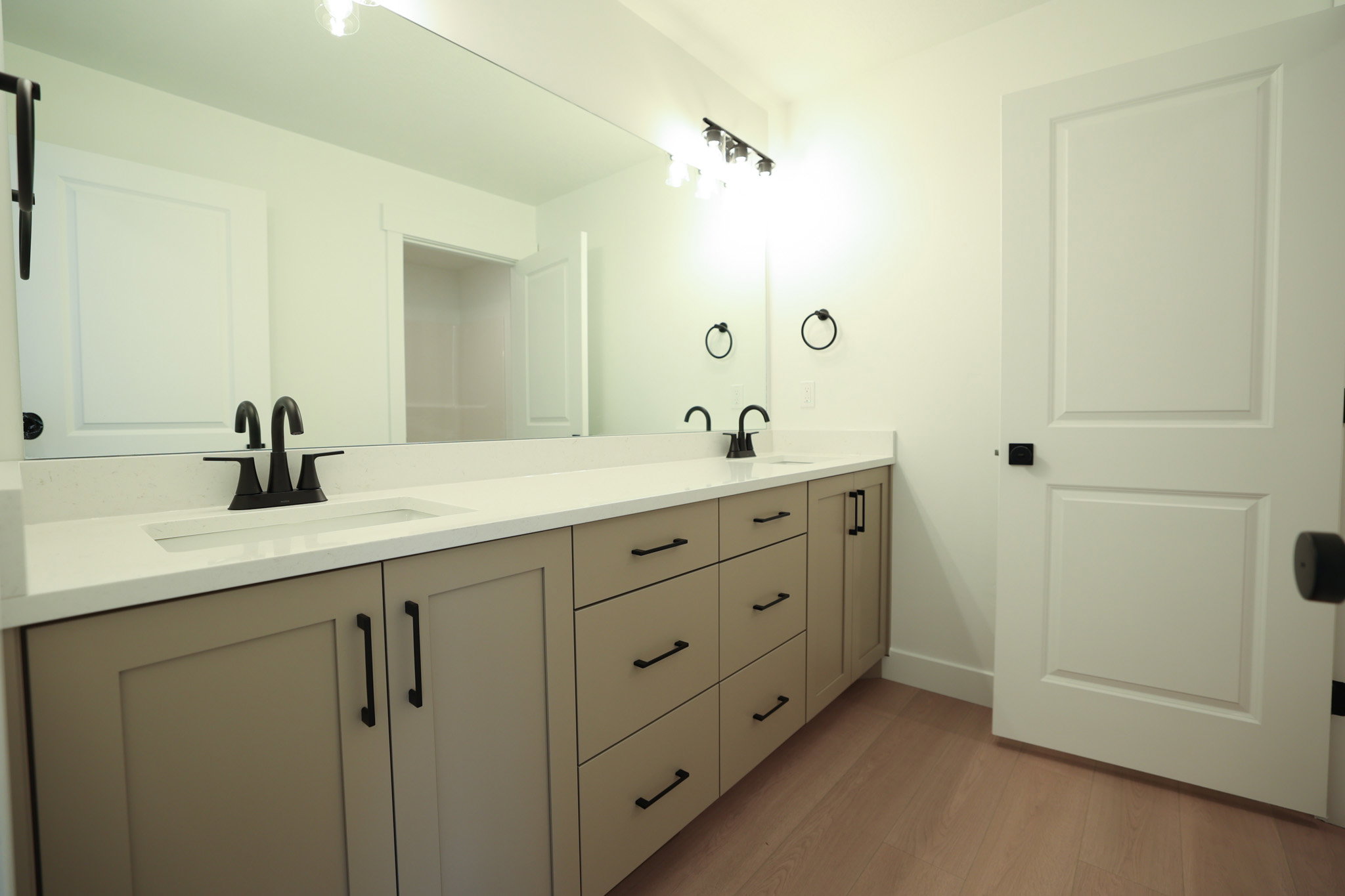 Dual vanity with matte black fixtures, light countertop, light wood-finish flooring, and shaker-style cabinetry