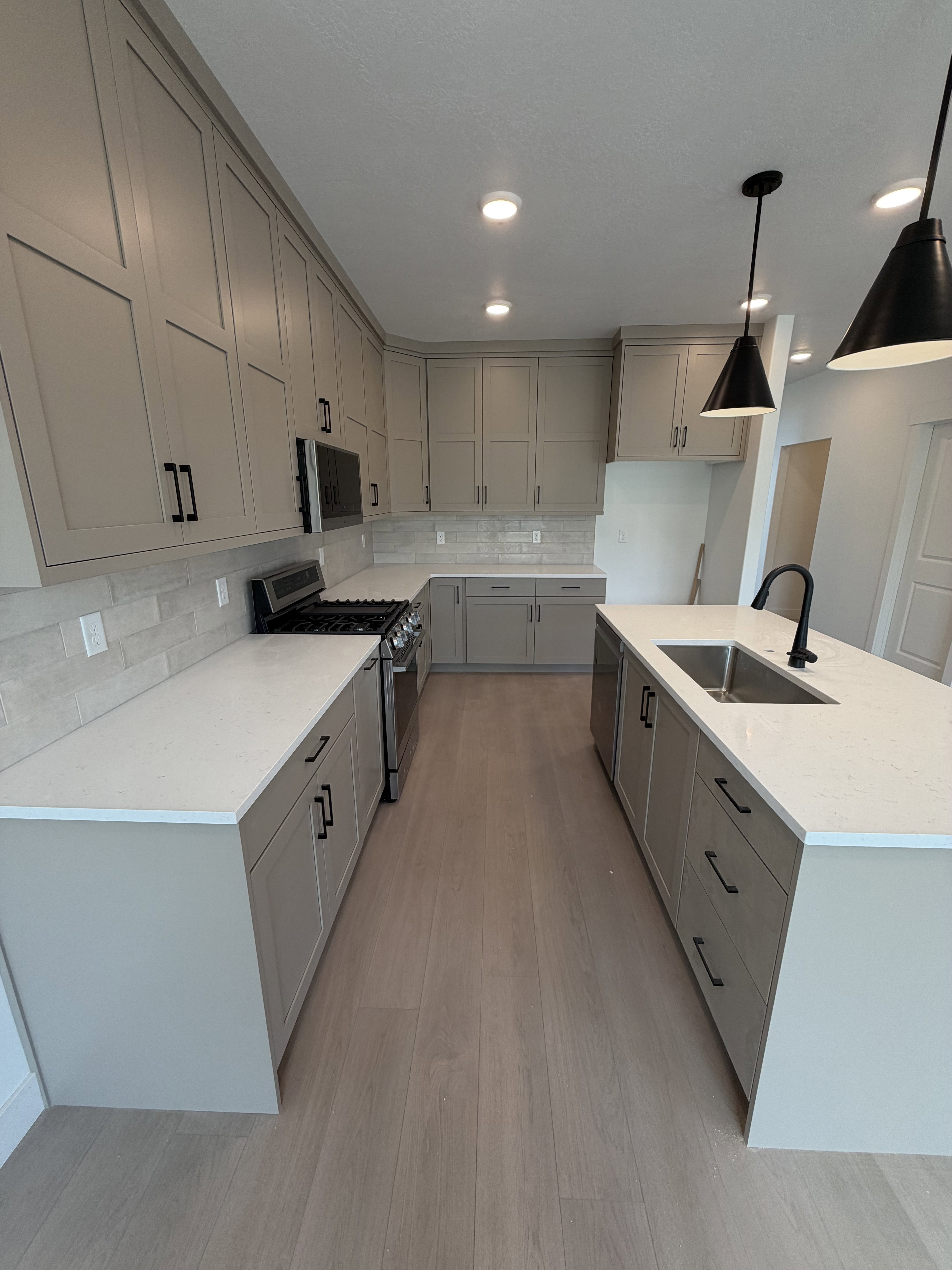 Kitchen featuring light gray cabinetry with black hardware, white countertops, wood-finish flooring, a stainless steel gas range, and a kitchen island with an undermount sink and pendant lighting