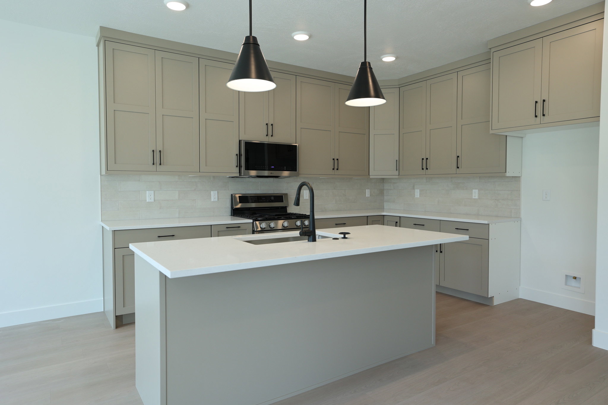 Modern kitchen featuring a central island with an integrated sink, light-toned cabinetry, light-colored countertops, a tile backsplash, and wood-finish flooring