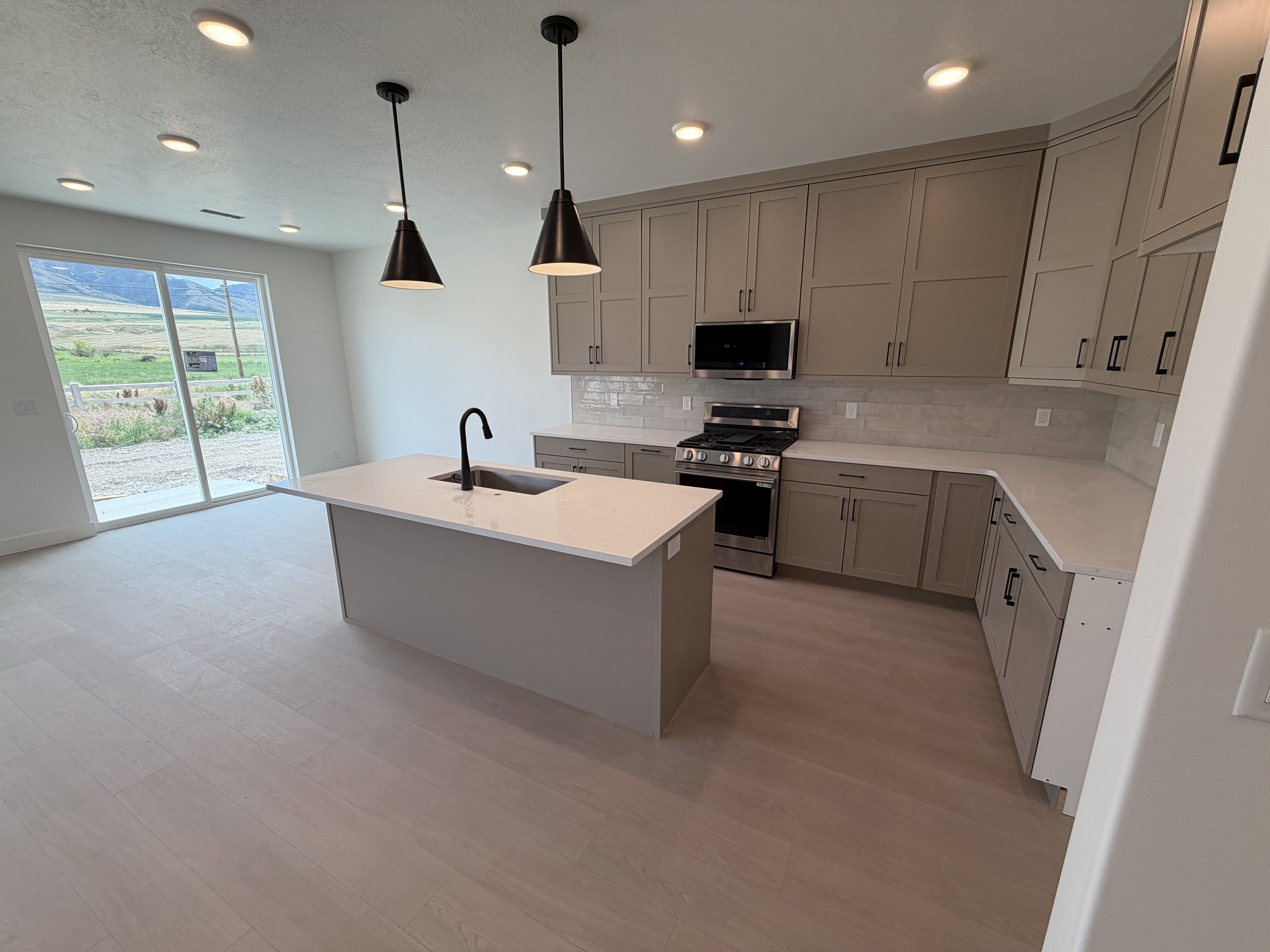 Open concept kitchen featuring light wood-finish flooring, a central island with an integrated sink and matte black faucet, and pendant lighting