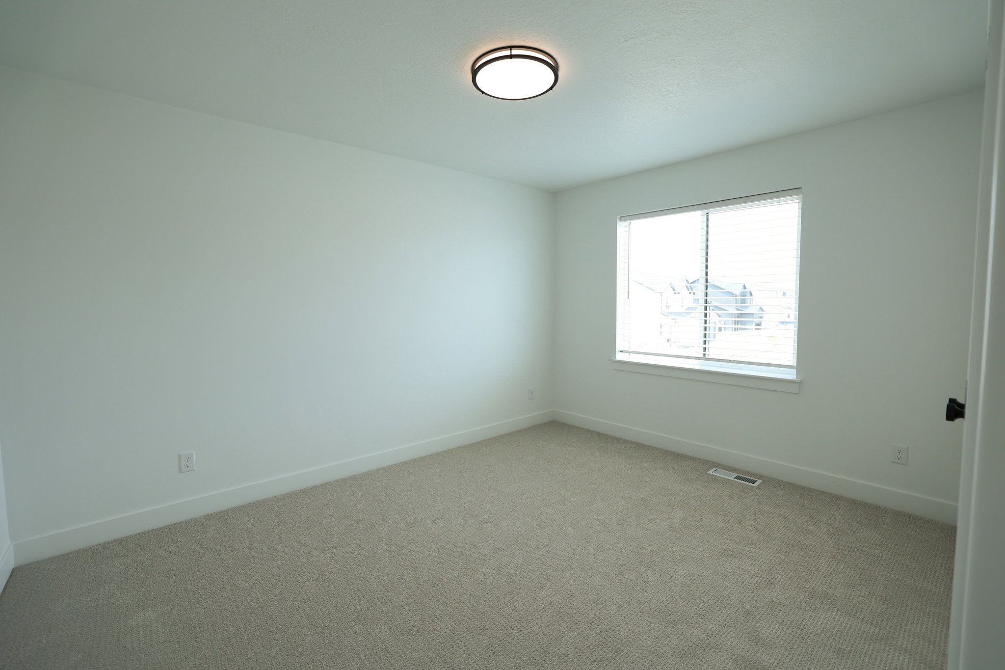 Bright room featuring a window with white blinds, neutral carpeting, white walls, and a modern flush-mount ceiling light