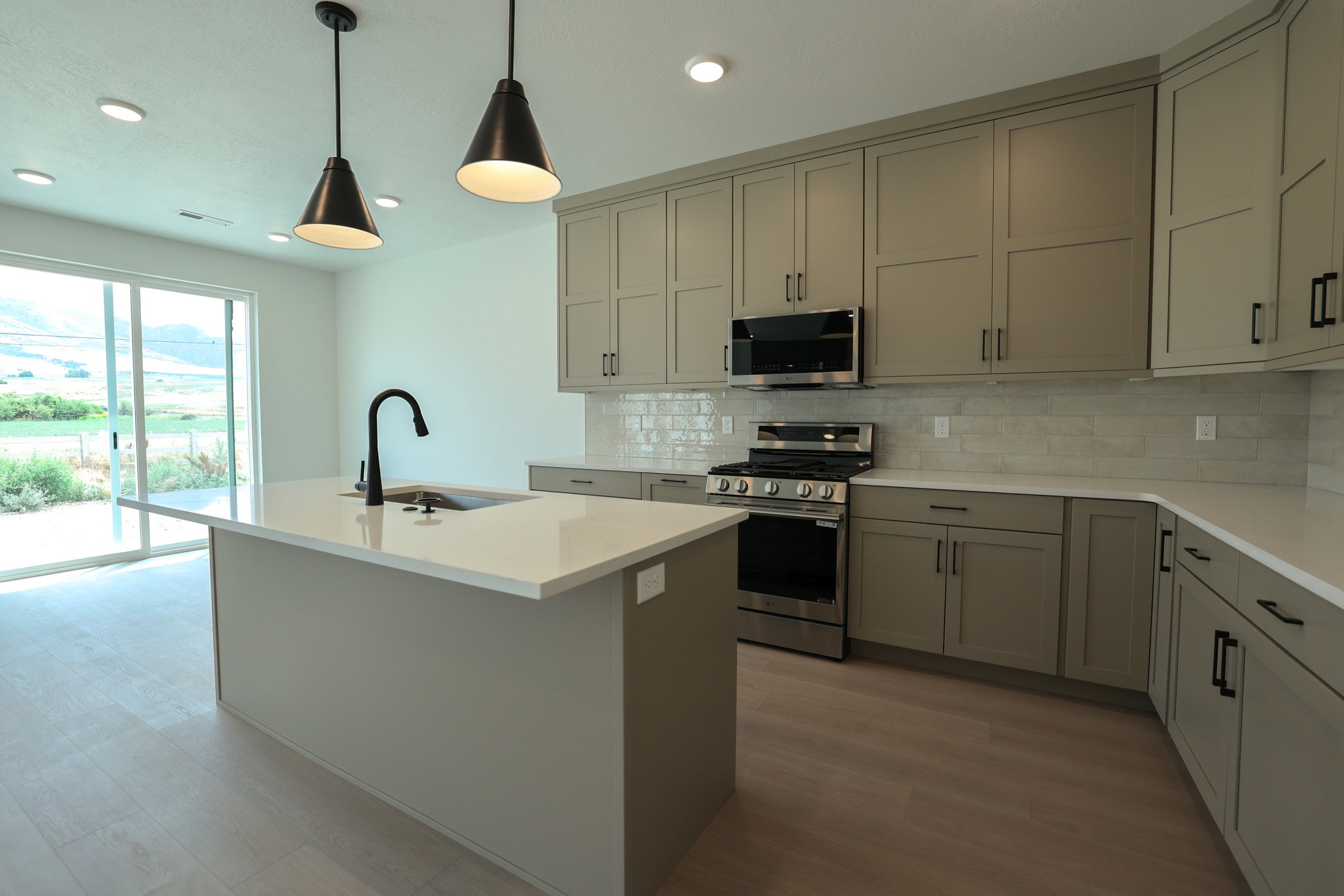 Modern kitchen featuring an island with a matte black gooseneck faucet, light-toned cabinetry, stainless steel appliances, white countertops, and a white subway tile backsplash