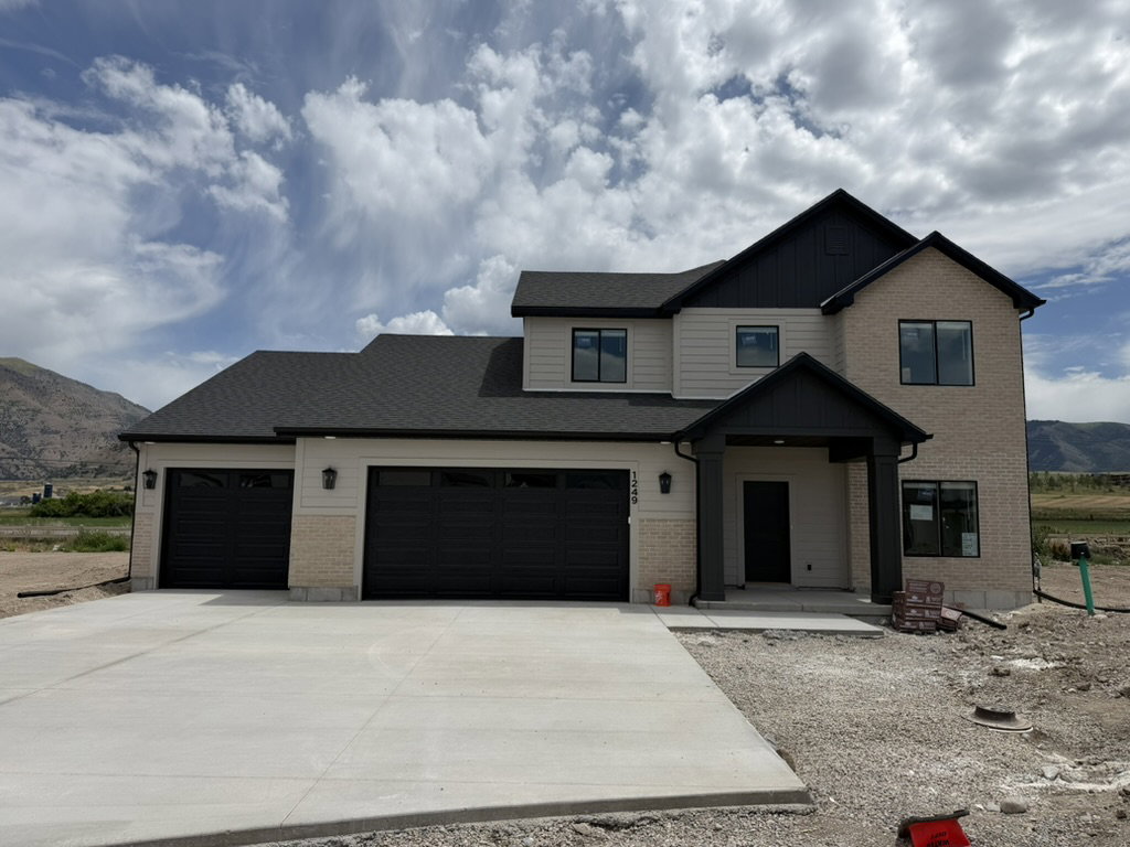 New construction residence featuring a light-colored brick and horizontal siding facade, dark roofing, and a prominent two-car garage with black doors