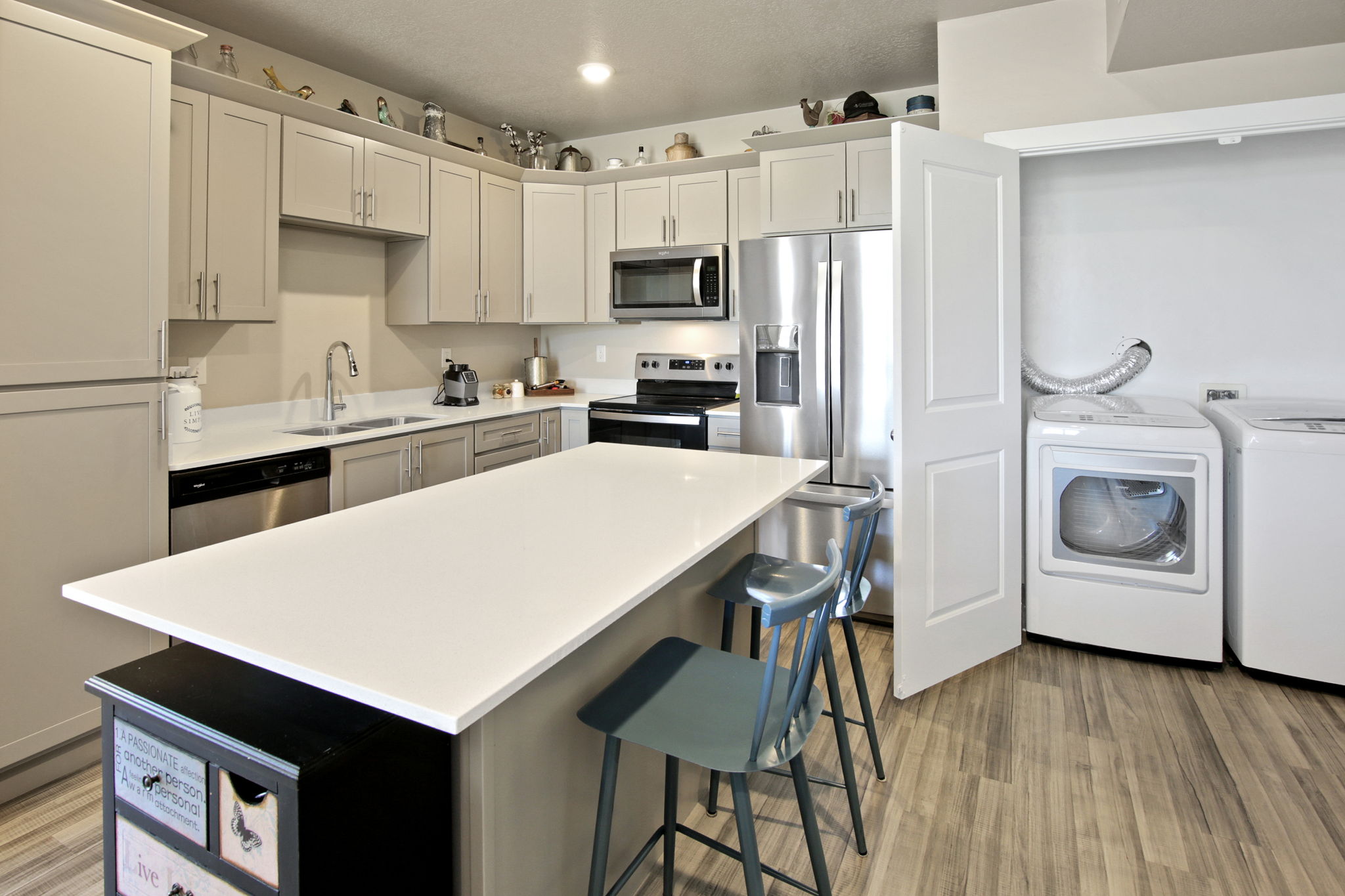 Kitchen featuring an island with white countertop, stainless steel appliances, light-toned cabinetry, and wood-finish flooring