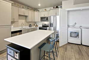 Kitchen featuring an island with white countertop, stainless steel appliances, light-toned cabinetry, and wood-finish flooring