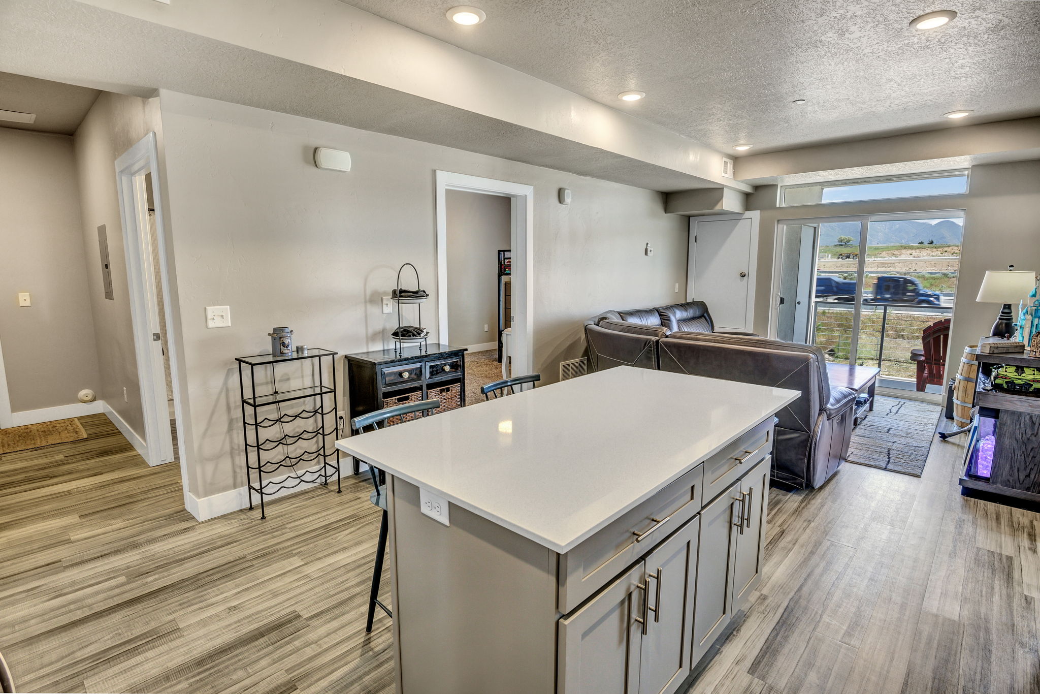 Central kitchen island with a light-toned countertop, wood-finish flooring, recessed lighting, neutral wall paint, and sliding glass doors to the exterior