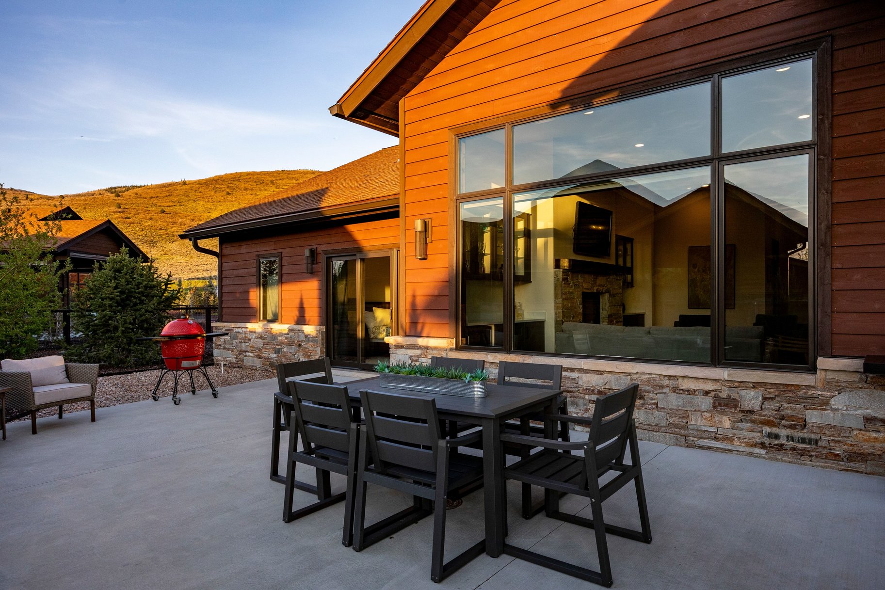 Spacious concrete patio featuring a large window, wood siding, natural stone accents, and exterior lighting fixtures