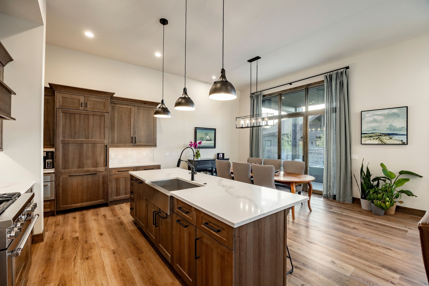 Gourmet kitchen and dining area featuring wood-finish flooring, custom wood cabinetry, a large kitchen island with a farmhouse sink, stainless steel appliances, and a wall of glass doors