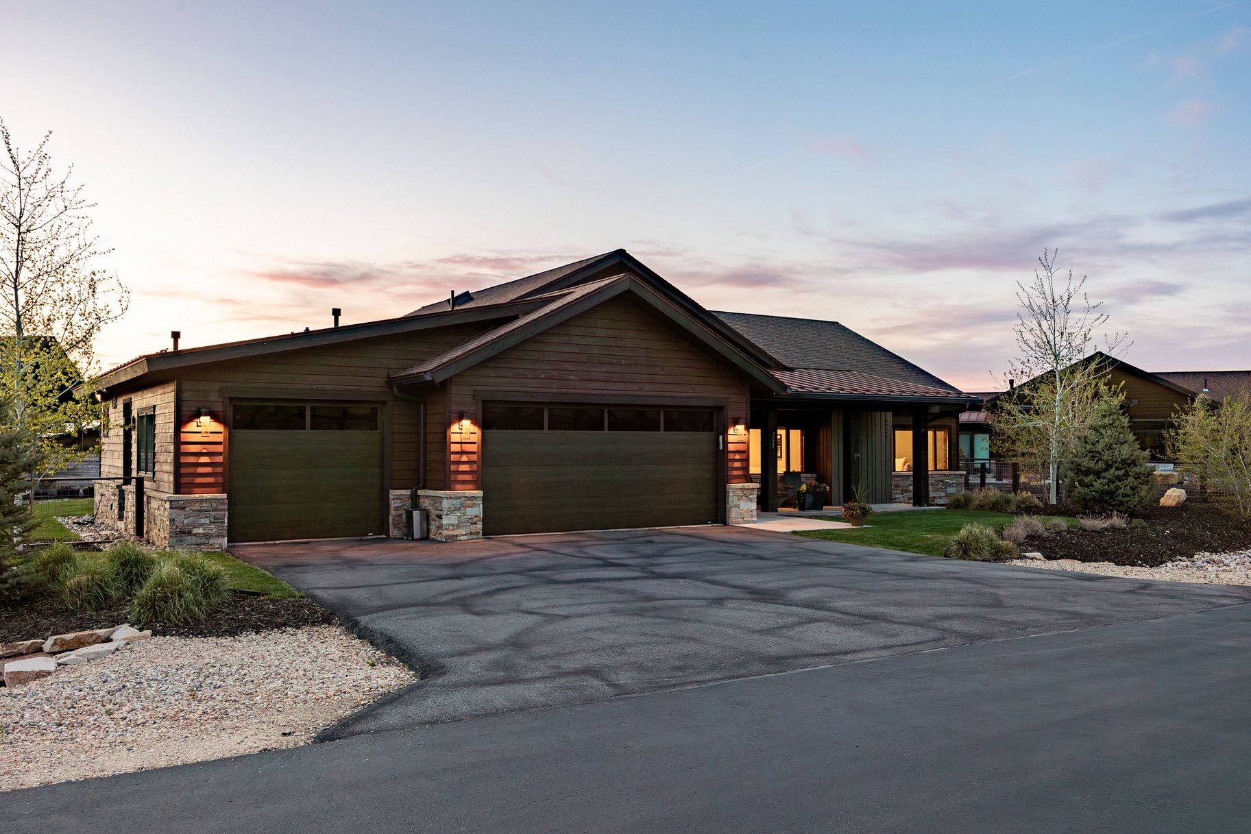 Ranch-style residence featuring a dark wood-finish exterior, stone accents, multiple garage bays, a paved driveway, and manicured landscaping